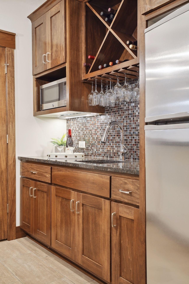 bar featuring dark stone countertops, sink, tasteful backsplash, and refrigerator