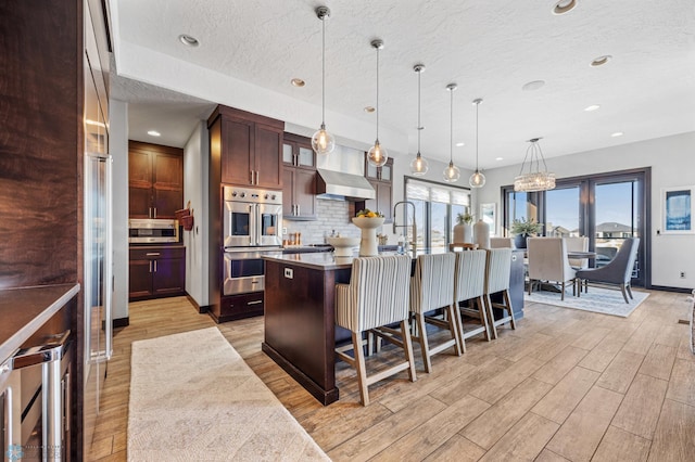 kitchen with appliances with stainless steel finishes, a kitchen breakfast bar, a kitchen island with sink, pendant lighting, and wine cooler