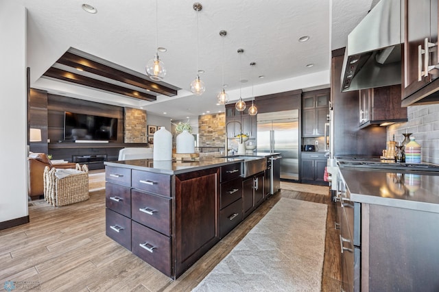 kitchen with high end appliances, a large island with sink, sink, decorative light fixtures, and dark brown cabinetry