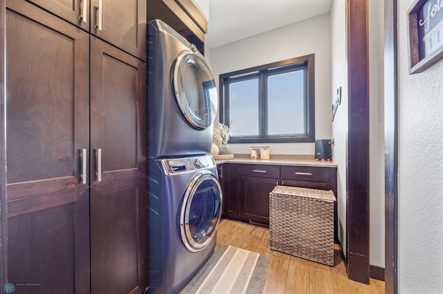 laundry room with cabinets, stacked washer / dryer, and light hardwood / wood-style flooring