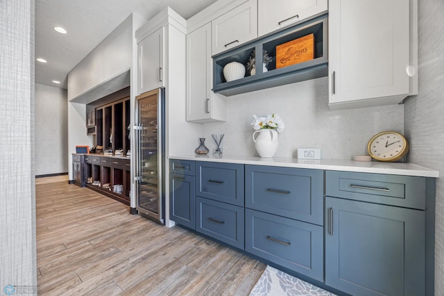 bar featuring blue cabinetry, white cabinetry, beverage cooler, and light wood-type flooring