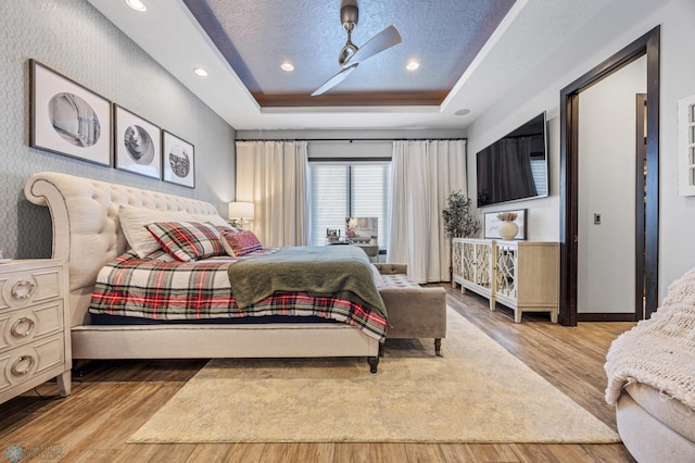 bedroom featuring a textured ceiling, light wood-type flooring, a tray ceiling, and ceiling fan