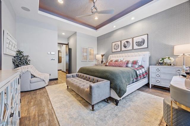 bedroom with ceiling fan, wood-type flooring, and a tray ceiling