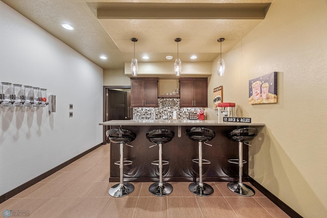 kitchen featuring backsplash, hanging light fixtures, light tile patterned floors, kitchen peninsula, and a breakfast bar area