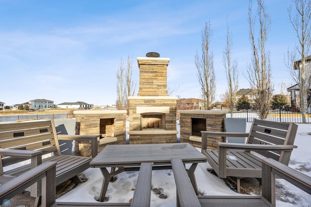 snow covered patio featuring an outdoor stone fireplace