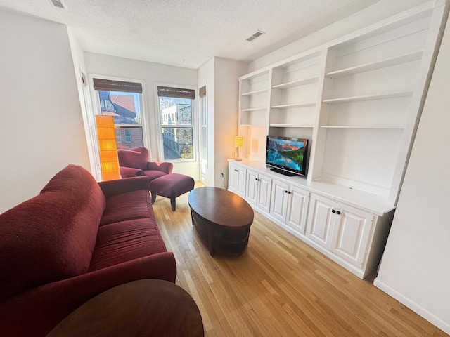 living room with a textured ceiling, light wood-type flooring, and built in shelves