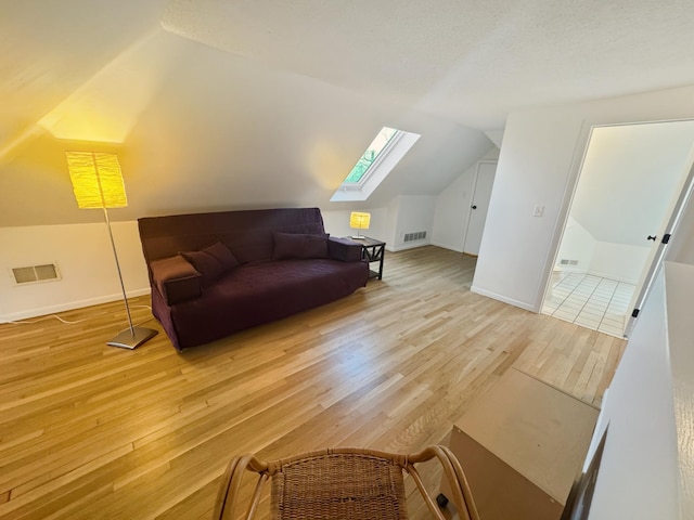 bonus room with vaulted ceiling with skylight and light wood-type flooring