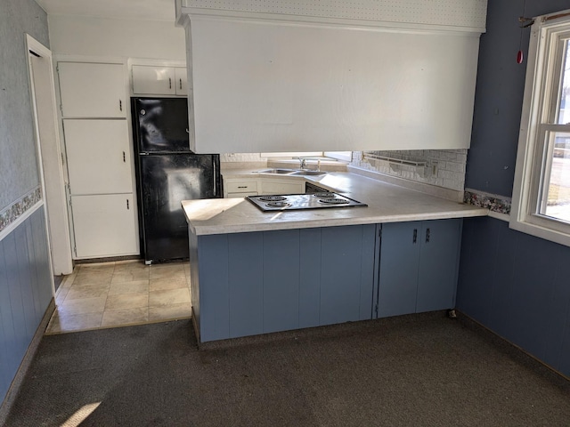 kitchen with white cabinetry, kitchen peninsula, black fridge, and sink