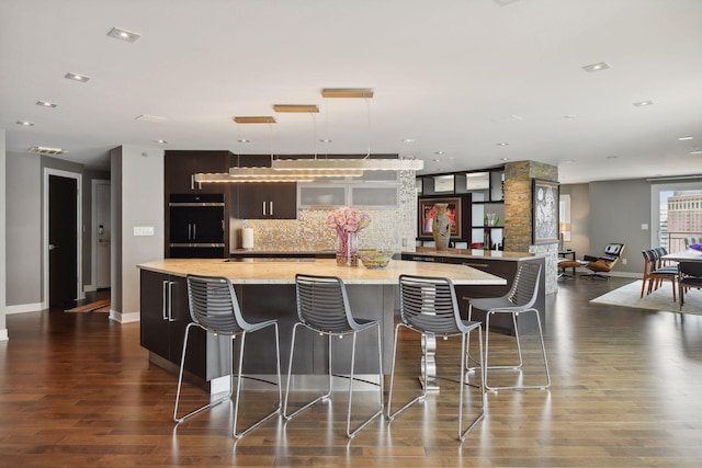 kitchen with decorative backsplash, dark hardwood / wood-style floors, a large island, light stone counters, and a breakfast bar area