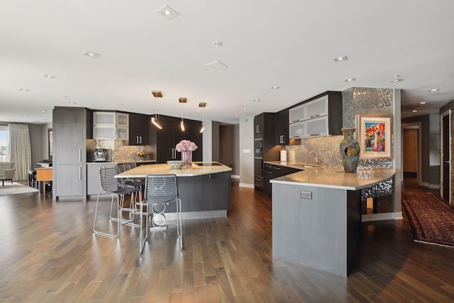 kitchen with decorative backsplash, kitchen peninsula, a breakfast bar, decorative light fixtures, and dark hardwood / wood-style floors