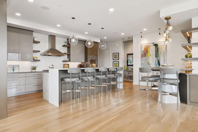 kitchen featuring pendant lighting, stainless steel oven, wall chimney exhaust hood, and a breakfast bar area