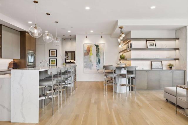 kitchen with a kitchen breakfast bar, light hardwood / wood-style floors, hanging light fixtures, and gray cabinetry