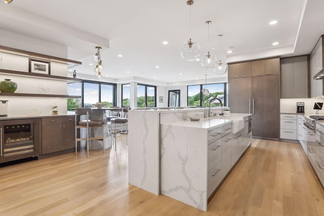 kitchen with sink, light stone countertops, decorative light fixtures, beverage cooler, and light wood-type flooring