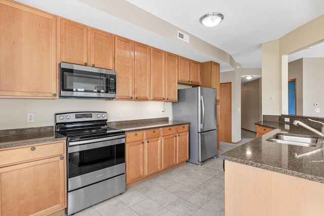 kitchen featuring sink, kitchen peninsula, dark stone countertops, light tile patterned floors, and appliances with stainless steel finishes