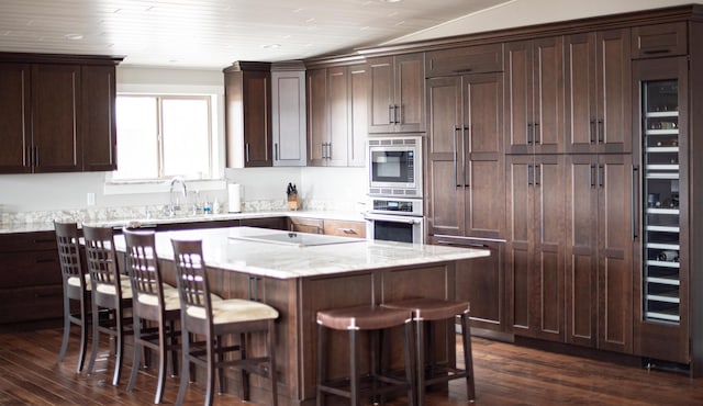 kitchen with a kitchen breakfast bar, light stone counters, dark brown cabinets, and stainless steel appliances