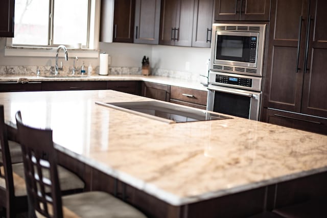 kitchen featuring sink, light stone counters, a kitchen bar, dark brown cabinetry, and stainless steel appliances