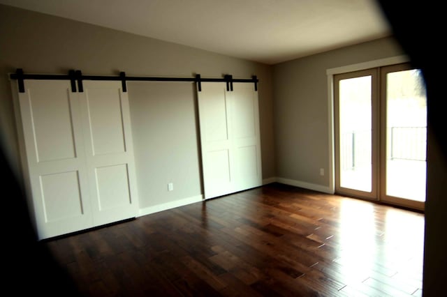 unfurnished bedroom with a barn door, dark wood-type flooring, and a closet