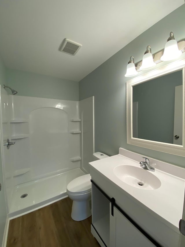 bathroom with hardwood / wood-style floors, a shower, toilet, and vanity