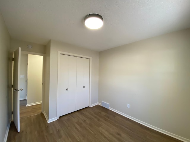 unfurnished bedroom with a closet, a textured ceiling, and dark hardwood / wood-style flooring