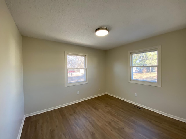 empty room with a healthy amount of sunlight, a textured ceiling, and dark hardwood / wood-style floors