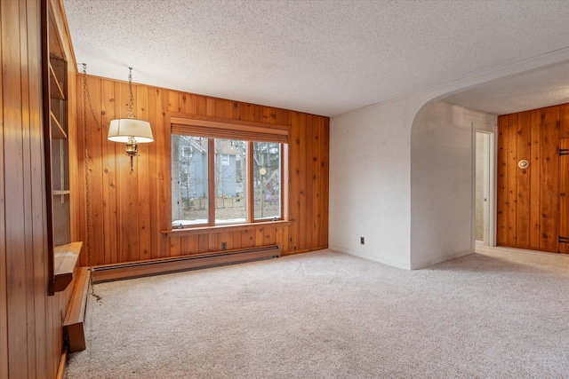 carpeted empty room with wood walls, a textured ceiling, and a baseboard heating unit