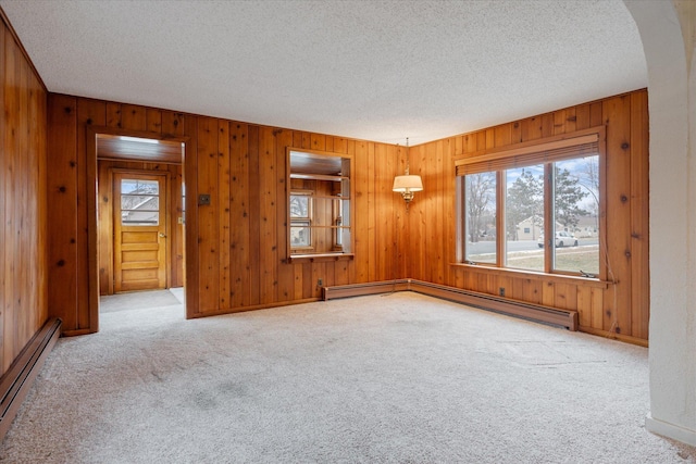 carpeted empty room featuring wooden walls, a textured ceiling, and baseboard heating