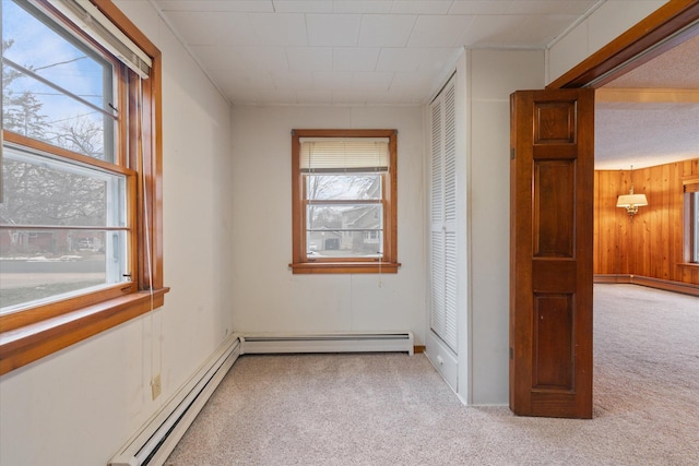 spare room featuring a baseboard heating unit, light carpet, and wood walls