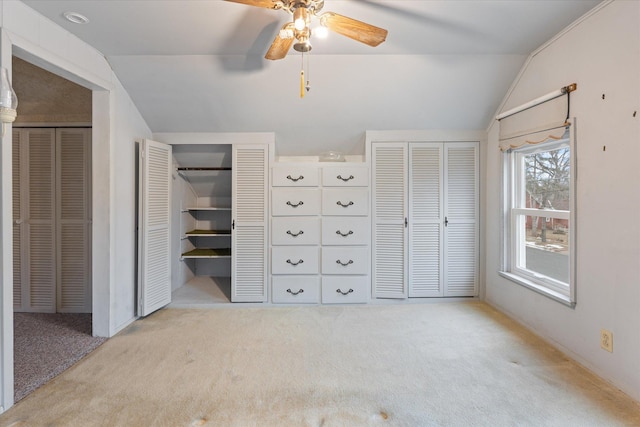 unfurnished bedroom featuring lofted ceiling, ceiling fan, light colored carpet, and multiple closets