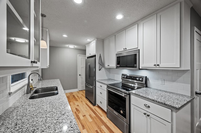 kitchen featuring tasteful backsplash, appliances with stainless steel finishes, light wood-type flooring, white cabinetry, and a sink