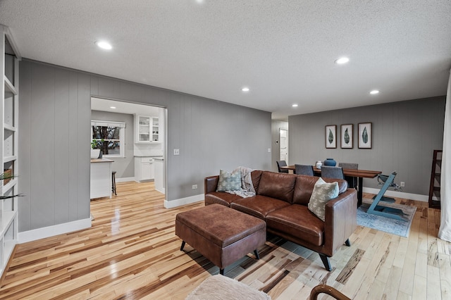 living area featuring light wood-type flooring, a textured ceiling, baseboards, and recessed lighting