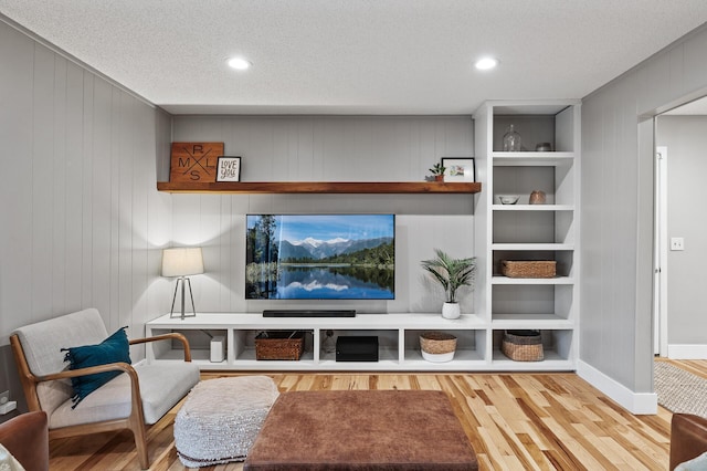 living area with a textured ceiling, built in shelves, recessed lighting, wood finished floors, and baseboards