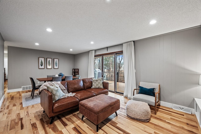 living room featuring visible vents, a textured ceiling, and light wood-style flooring