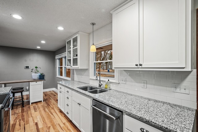 kitchen featuring light wood finished floors, tasteful backsplash, stainless steel dishwasher, white cabinets, and a sink