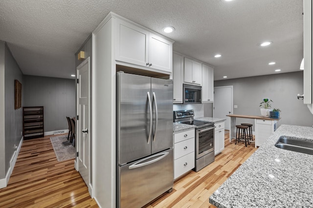 kitchen featuring light wood-style flooring, light stone countertops, stainless steel appliances, white cabinetry, and a sink