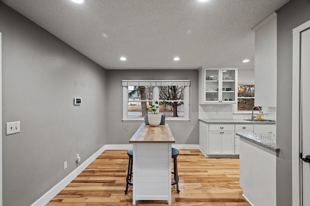 kitchen with glass insert cabinets, light wood-type flooring, a sink, and white cabinetry