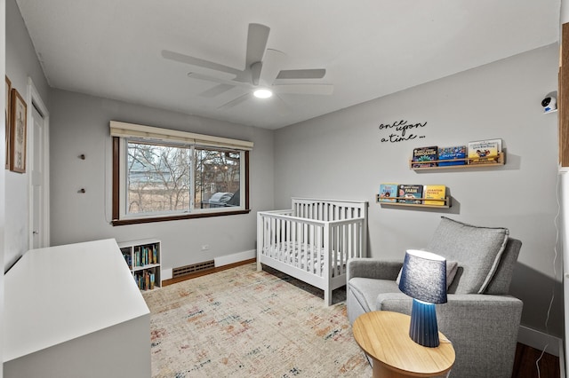 bedroom with visible vents, baseboards, a ceiling fan, wood finished floors, and a nursery area