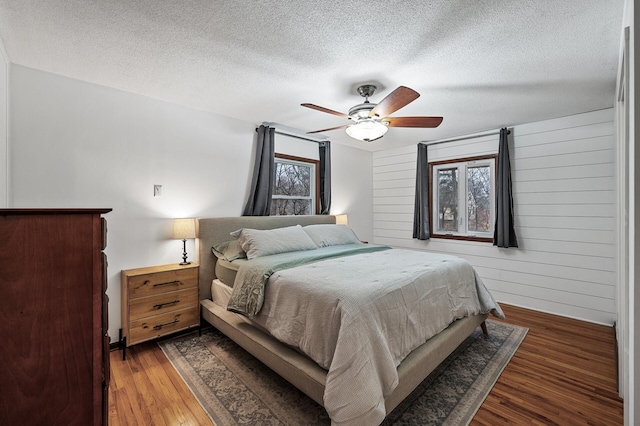 bedroom with wood walls, a textured ceiling, and wood finished floors