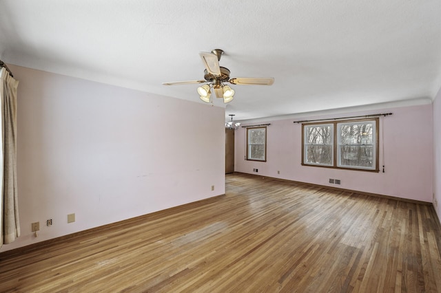 empty room featuring ceiling fan with notable chandelier and light wood-type flooring