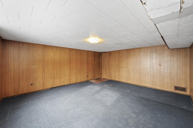 carpeted empty room featuring wooden walls