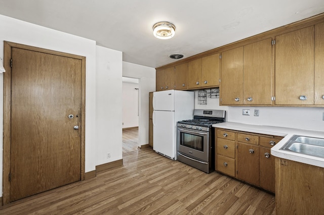 kitchen with white refrigerator, stainless steel gas range oven, sink, and light hardwood / wood-style floors