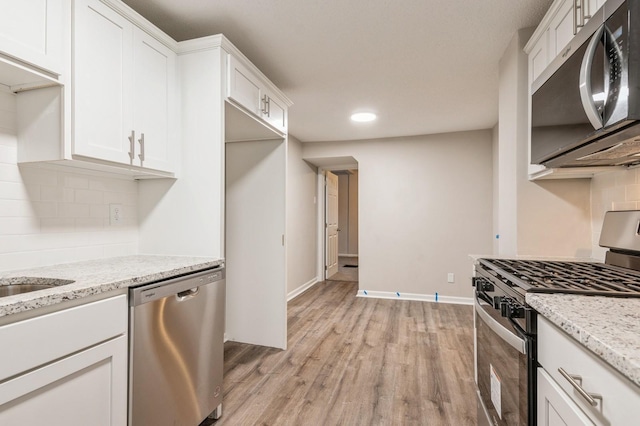 kitchen featuring stainless steel appliances, light stone counters, backsplash, light hardwood / wood-style floors, and white cabinets