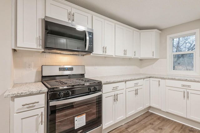 kitchen with light stone counters, light wood-type flooring, white cabinetry, and stainless steel appliances