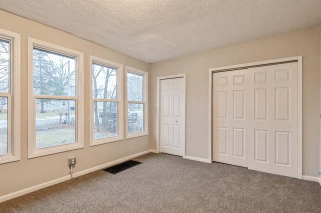 unfurnished bedroom featuring multiple closets, carpet, and a textured ceiling