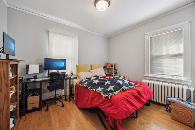 bedroom with hardwood / wood-style floors, ornamental molding, radiator heating unit, and multiple windows