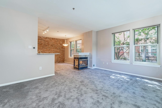 unfurnished living room featuring brick wall, a multi sided fireplace, rail lighting, and a wealth of natural light