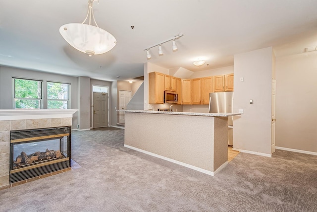 kitchen featuring light carpet, stainless steel appliances, a tile fireplace, light brown cabinets, and decorative light fixtures