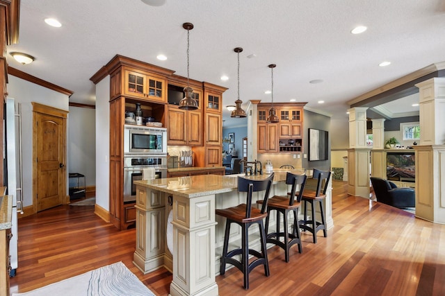 kitchen featuring appliances with stainless steel finishes, light wood-type flooring, light stone counters, ornamental molding, and decorative light fixtures