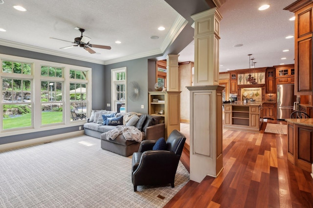 living room featuring ceiling fan, ornate columns, a textured ceiling, ornamental molding, and dark hardwood / wood-style flooring