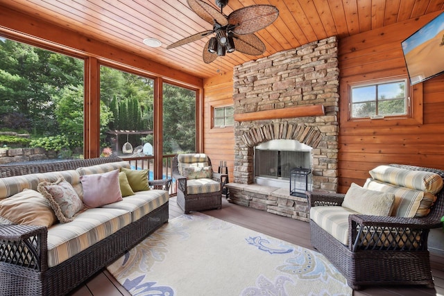 sunroom / solarium featuring a stone fireplace, ceiling fan, and wood ceiling