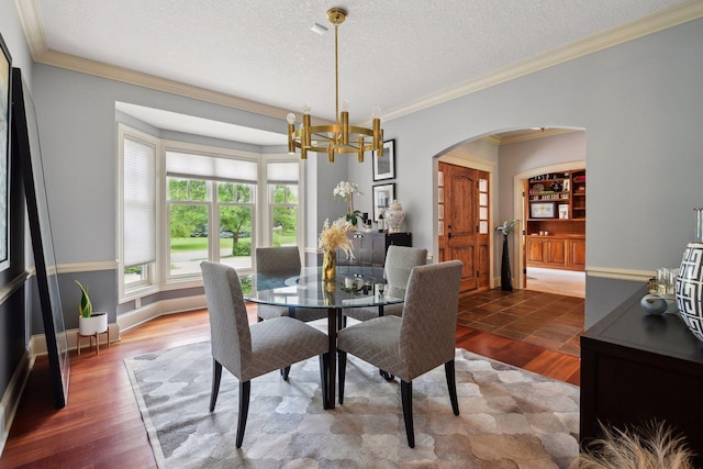 dining room with dark hardwood / wood-style floors, ornamental molding, a textured ceiling, and an inviting chandelier